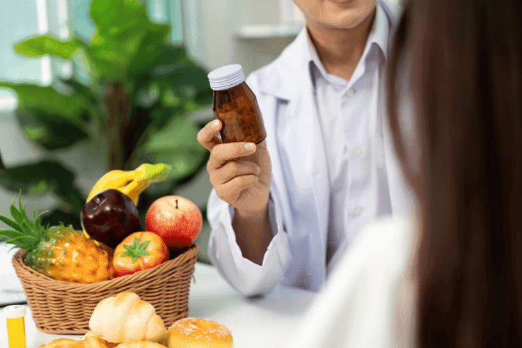 Doctor holding a brown supplement bottle near a basket of fresh fruits.